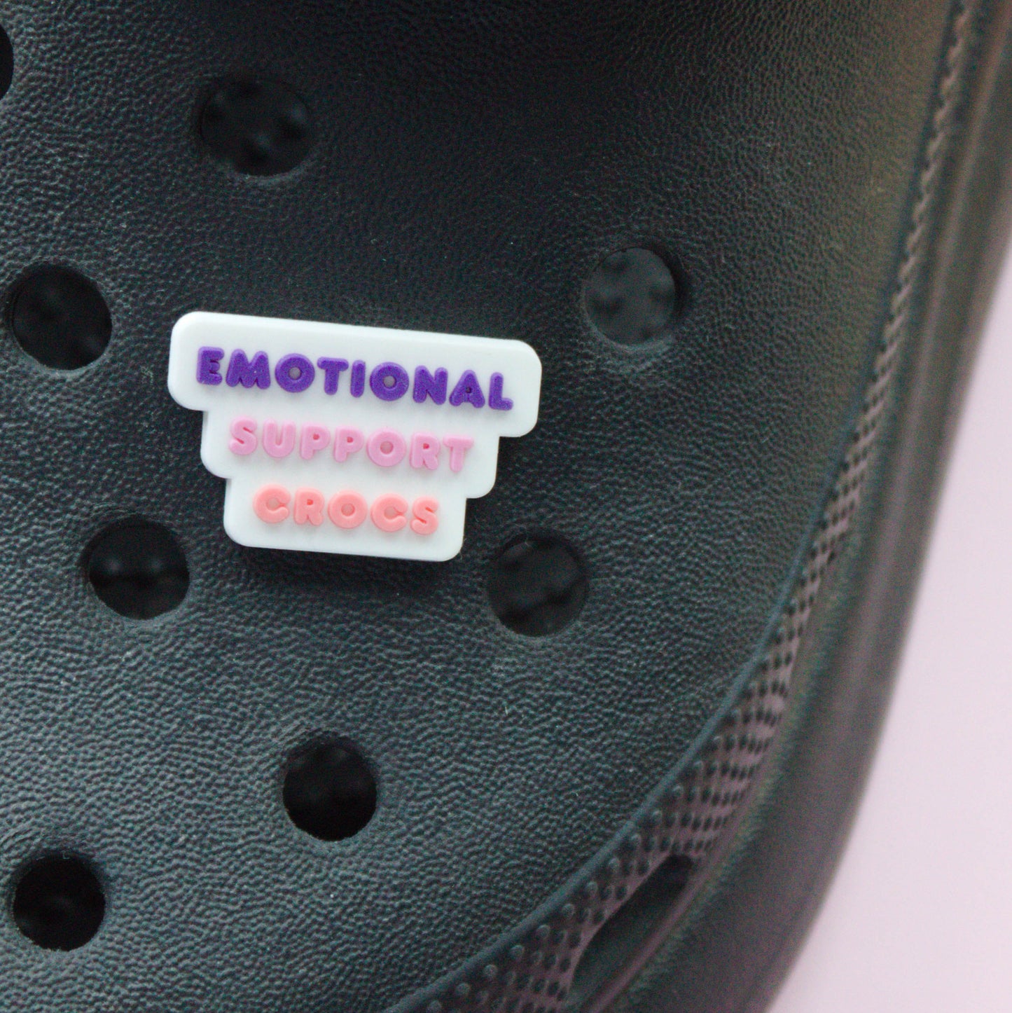 Emotional Support Crocs Slogan croc like shoe charm. White, pink and purple. Modelled on a black croc shoe.