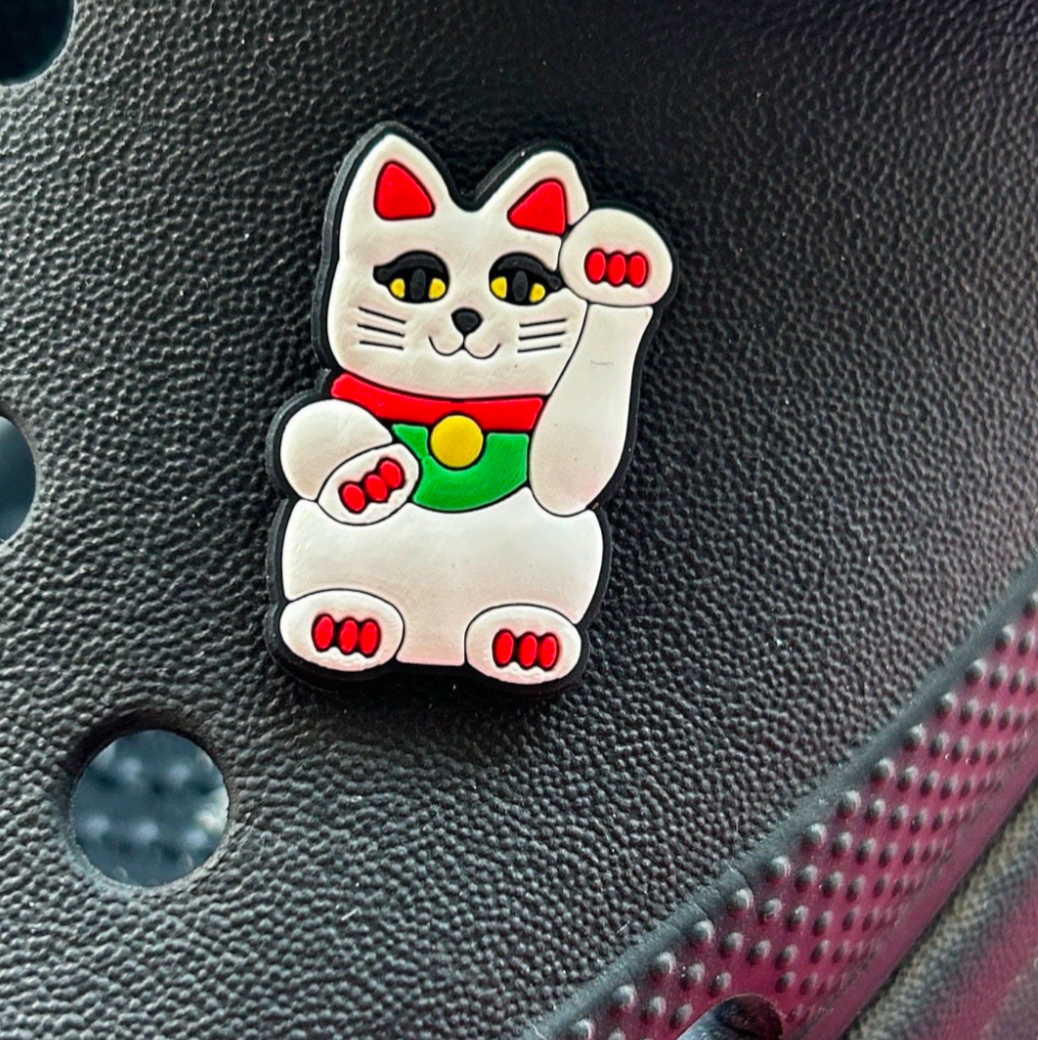 White lucky cat croc like shoe charm modelled on a black croc shoe.