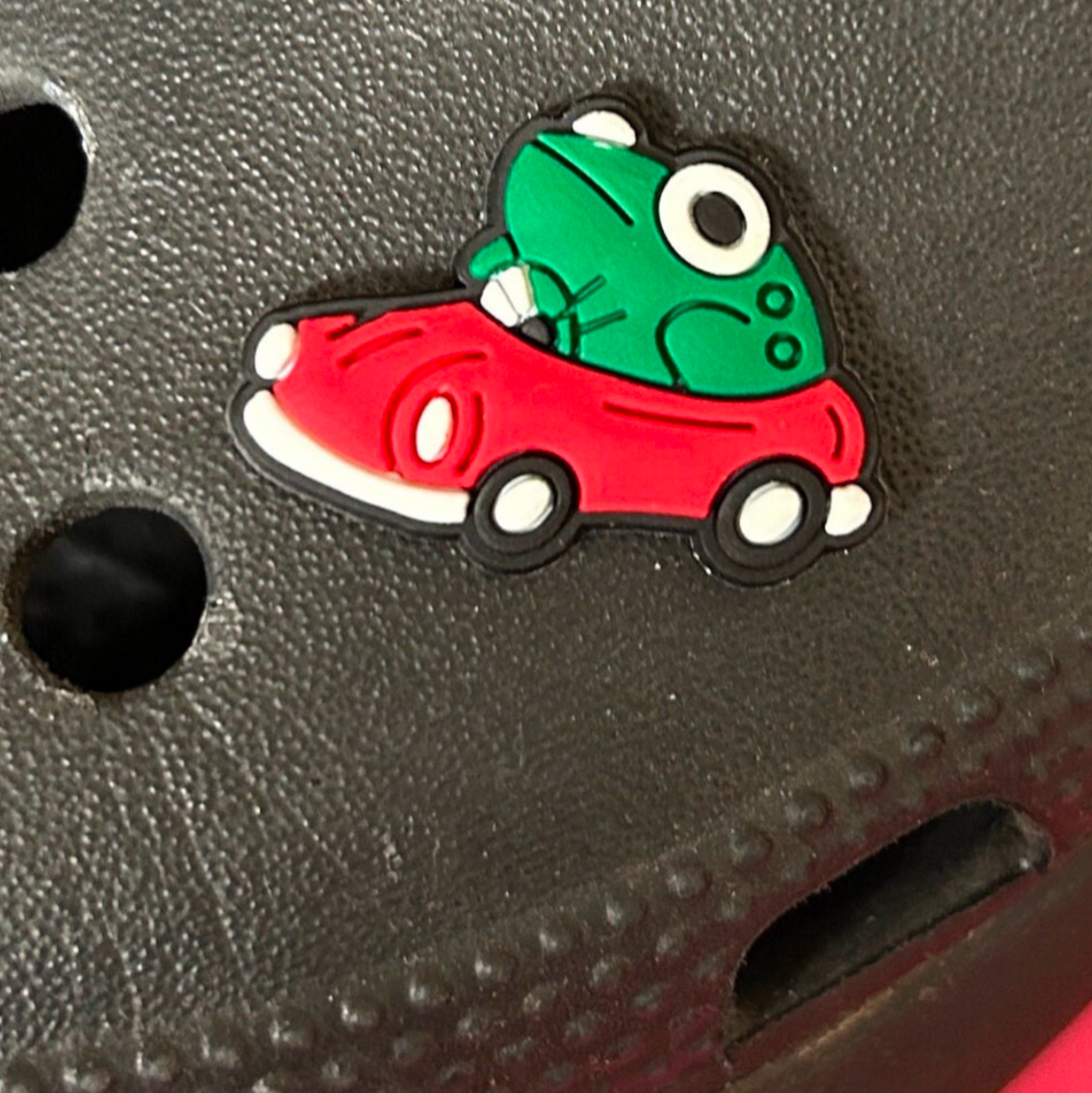 Frog driving a red car croc like shoe charm. Shown on a black croc shoe.