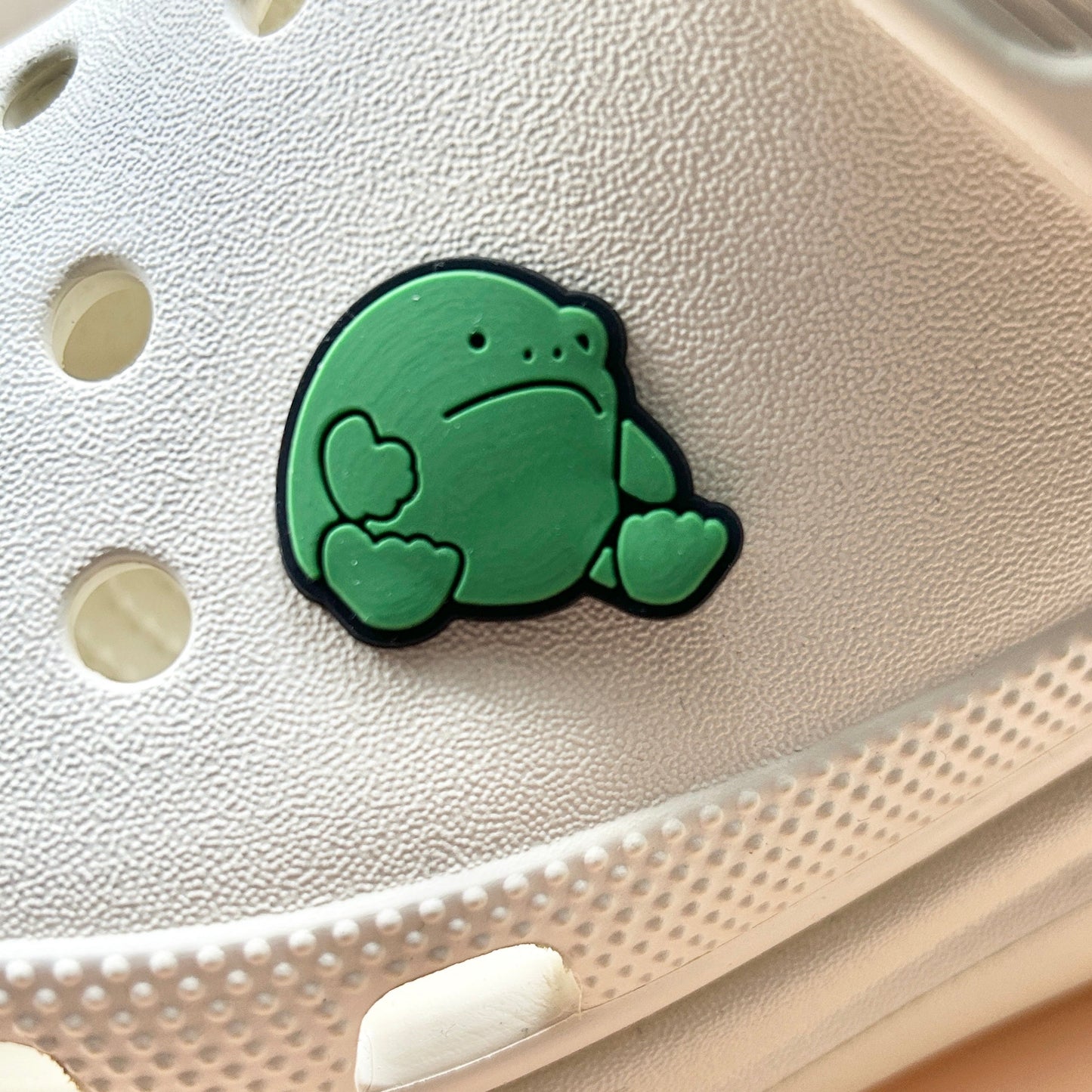 Green Grumpy Frog croc like shoe charm. Shown on a cream croc shoe.