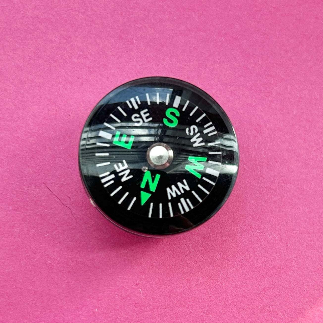 3D working compass croc shoe charm. Shown top down on a pink background.