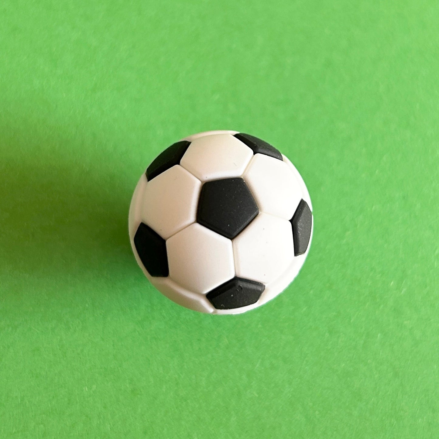 3D White and Black football croc shoe charm. Sport. Top down view on a green background.
