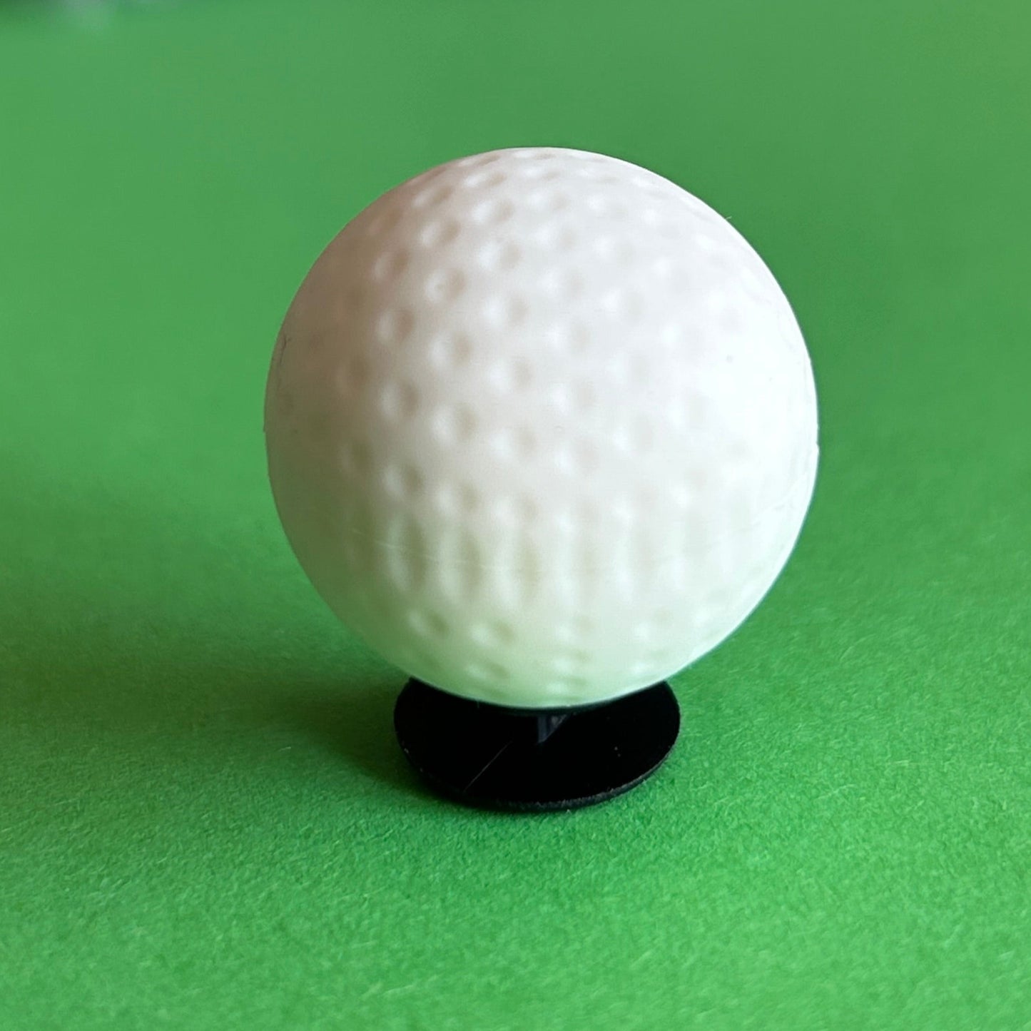 3D Golf Ball Croc shoe charm. White. Shown on a green background.