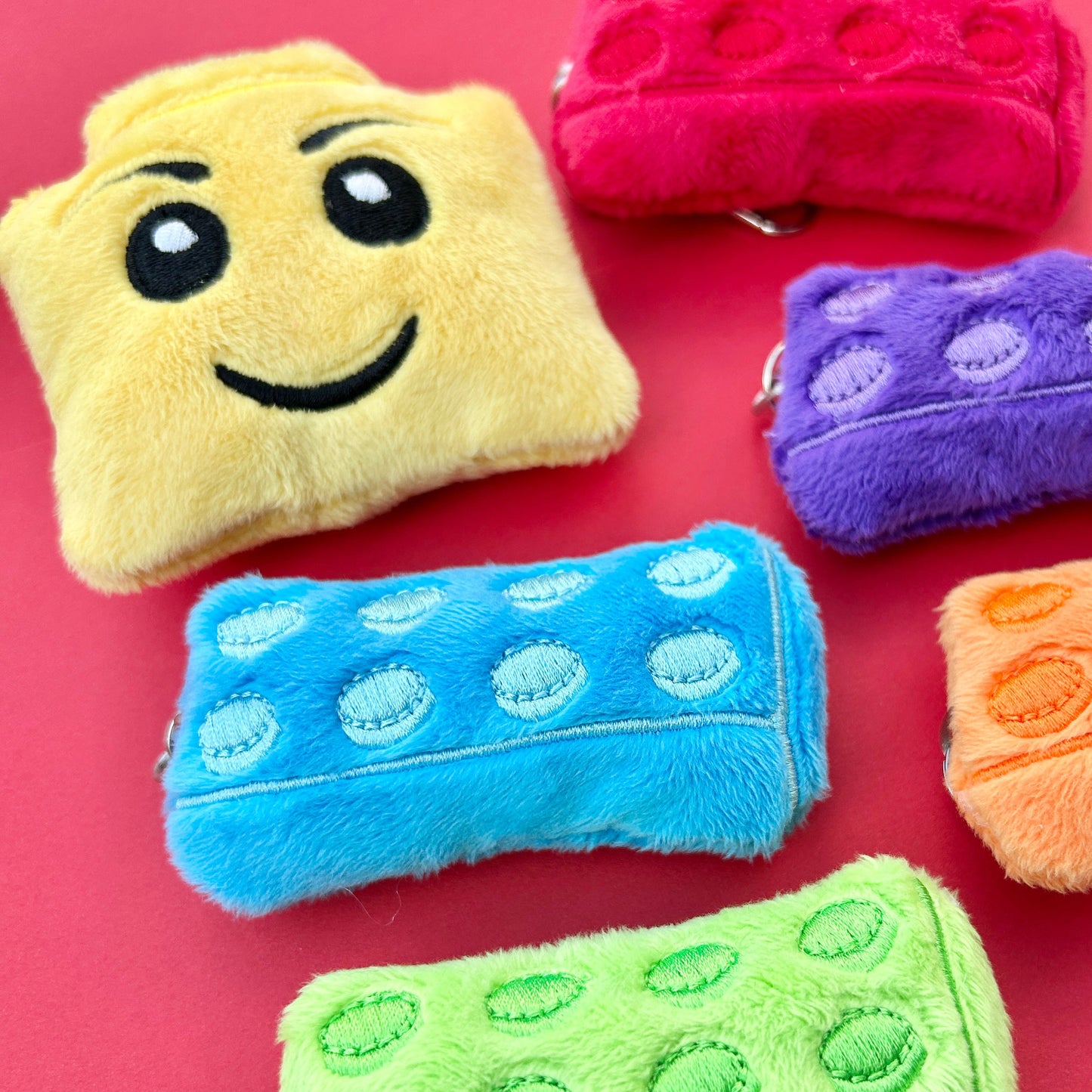 Colorful plush keyrings resembling building blocks on a red surface.