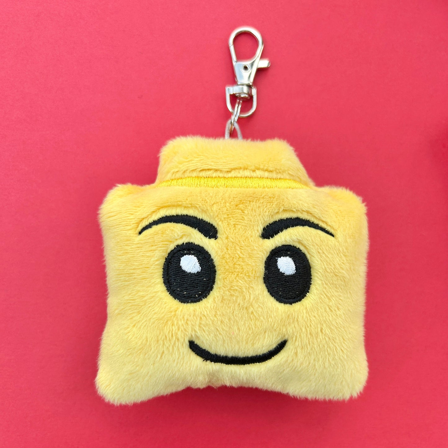 Plush keychain with a smiling face design on a red background.