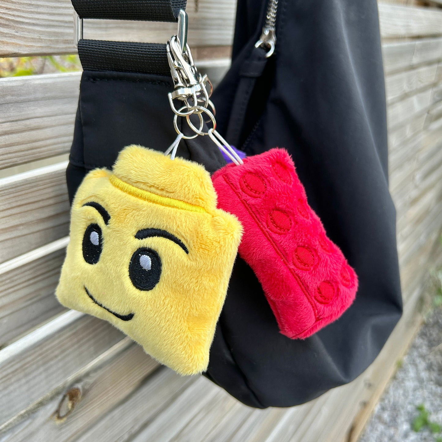 Plush keychains shaped like a yellow square with a face and a red circle with a dot, attached to a black bag.