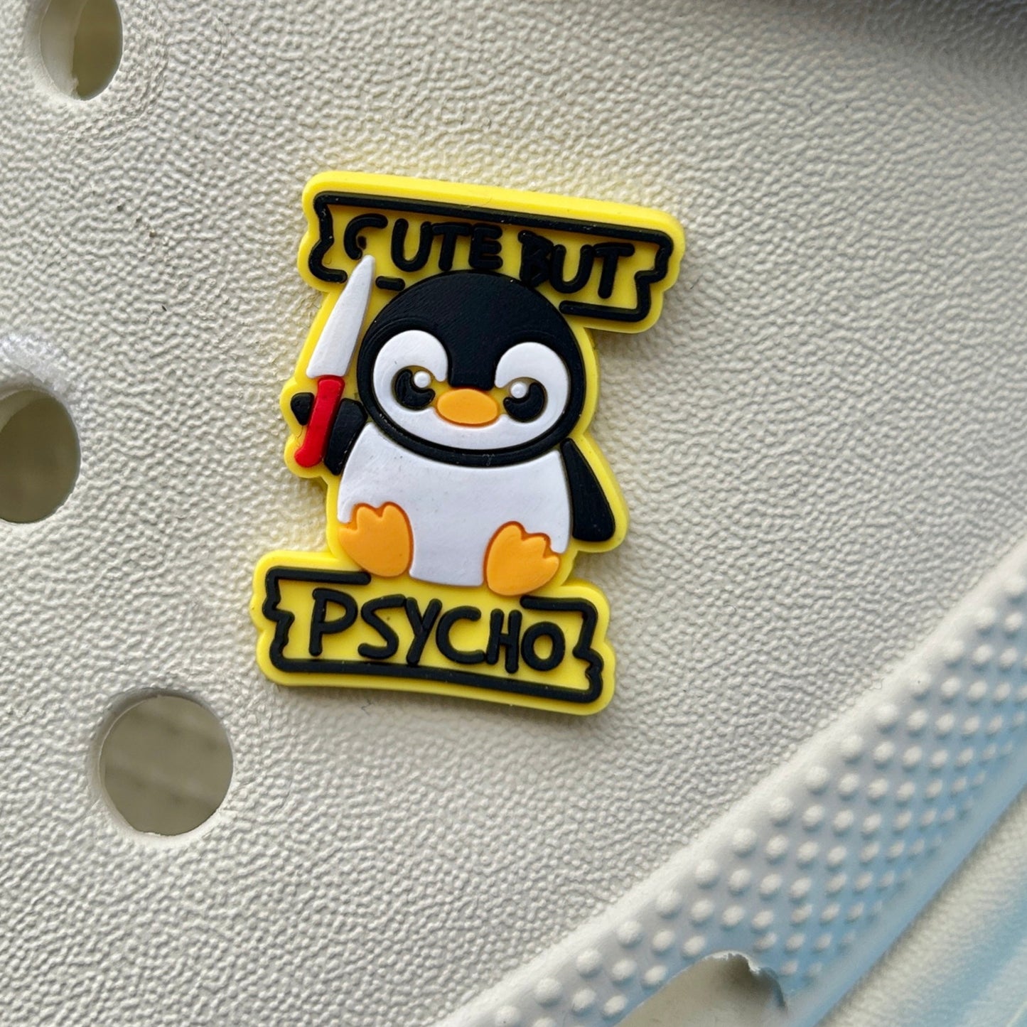 White shoe with a penguin-themed croc badge labeled 'Cute but Psycho' on a yellow background