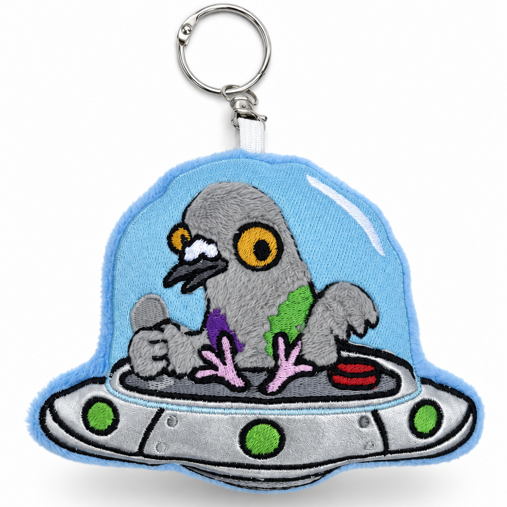 An embroidered keychain featuring a gray pigeon sitting inside a silver UFO with a light blue dome, attached to a silver metal key ring, on a white background.