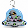 An embroidered keychain featuring a gray pigeon sitting inside a silver UFO with a light blue dome, attached to a silver metal key ring, on a white background.