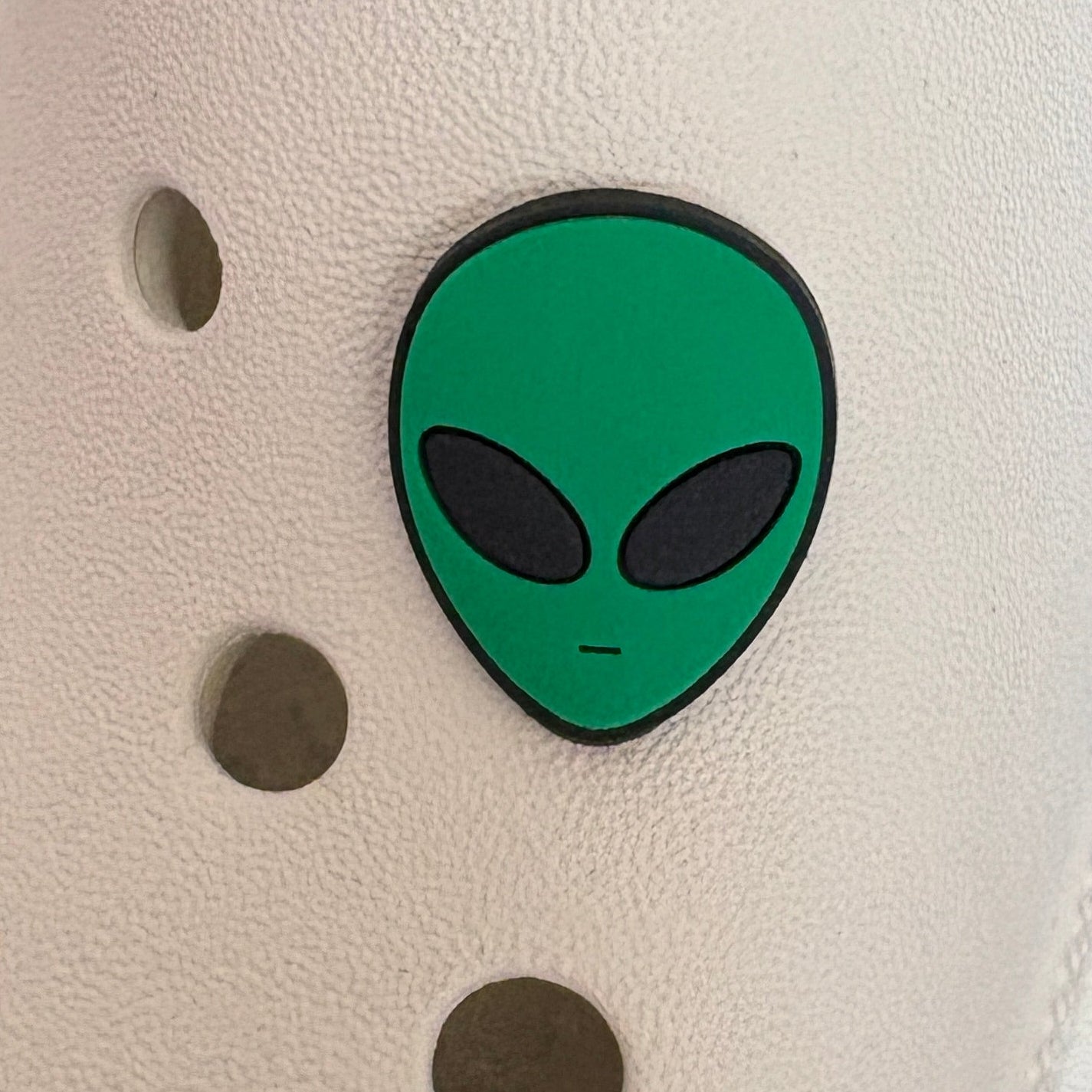 White shoe with a green alien shoe charm on a blurred background