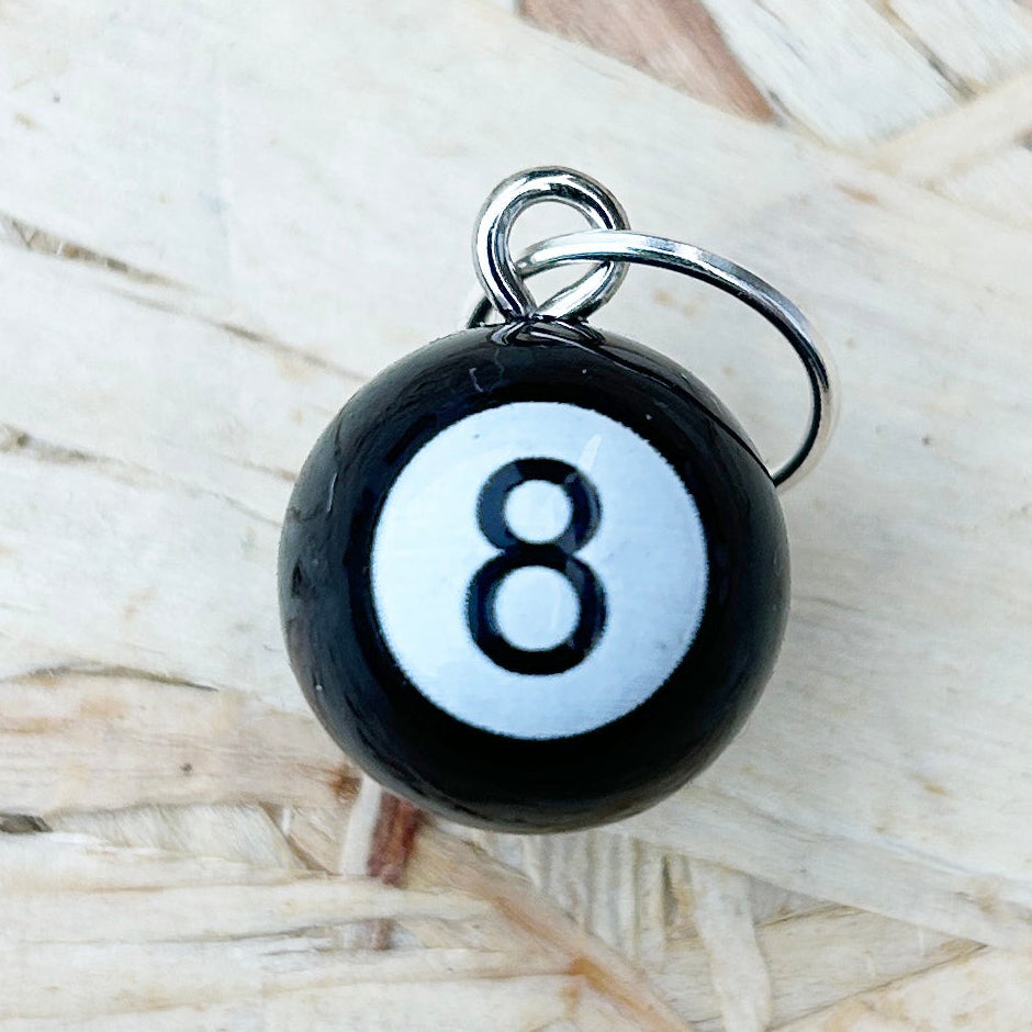 Black and white eight-ball stitch marker on a textured wood surface