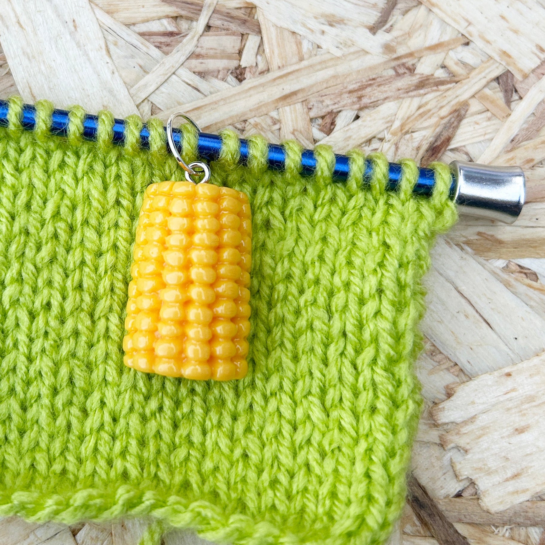 Green knitted fabric with knitting needles and a yellow stitch marker on a wooden surface