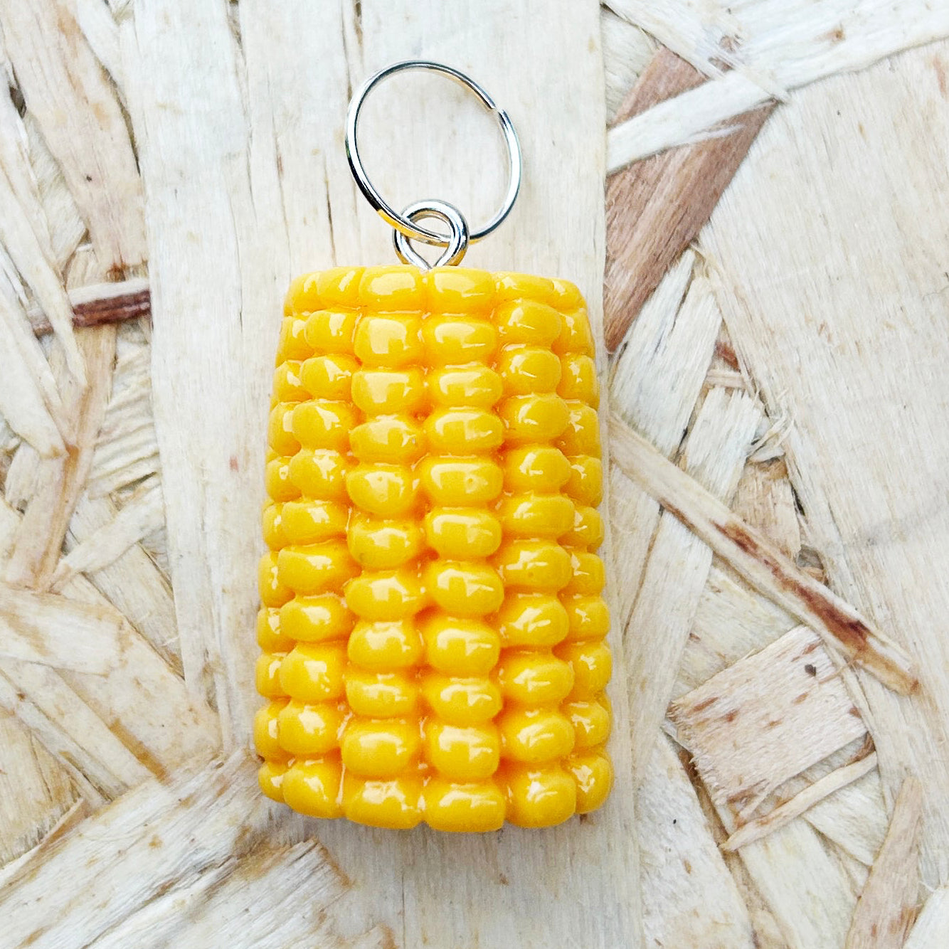 Yellow corn-shaped stitch marker on a straw background