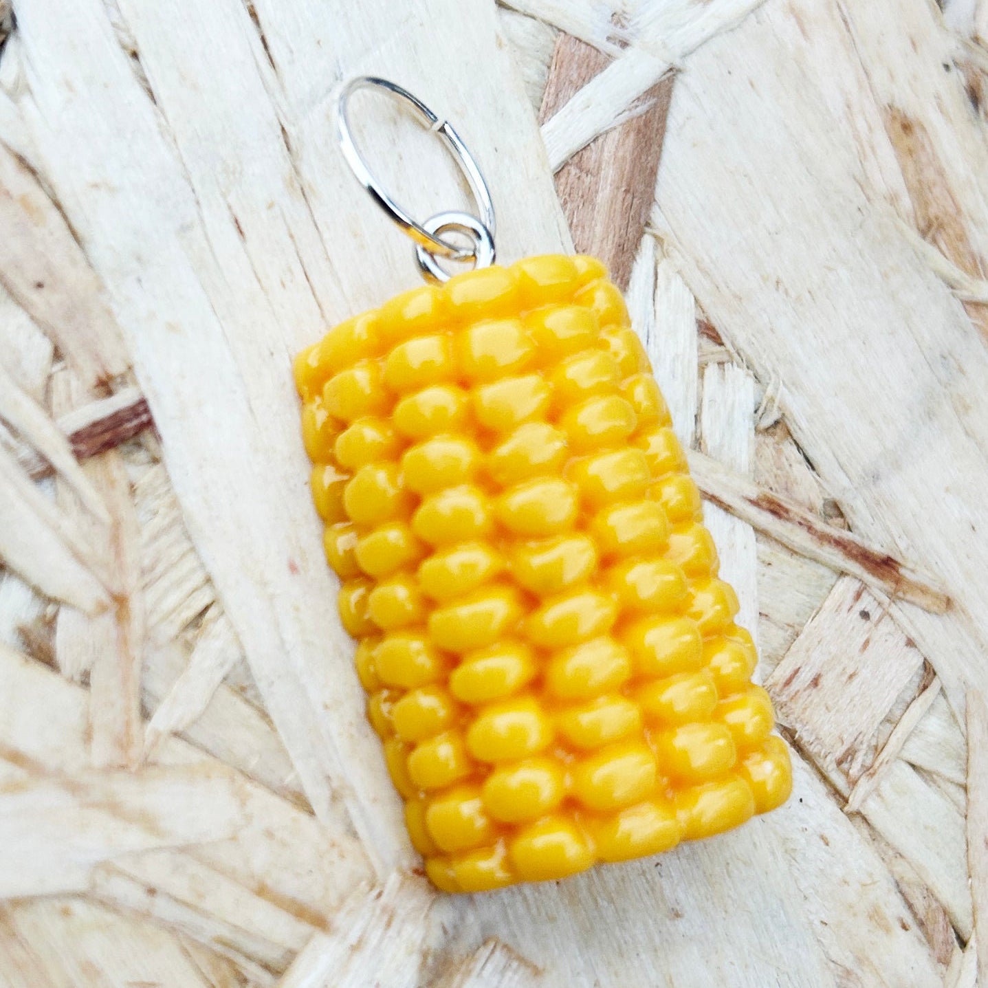 Yellow corn-shaped stitch marker on a straw background