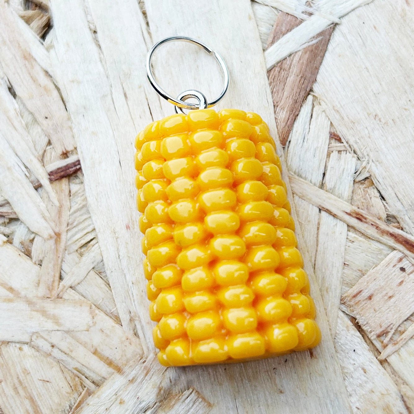 Yellow corn-shaped stitch marker on a textured wood background