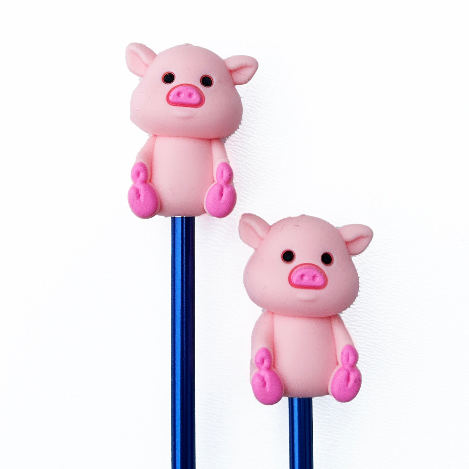 Two pink pig-shaped beads on blue knitting needles against a white background