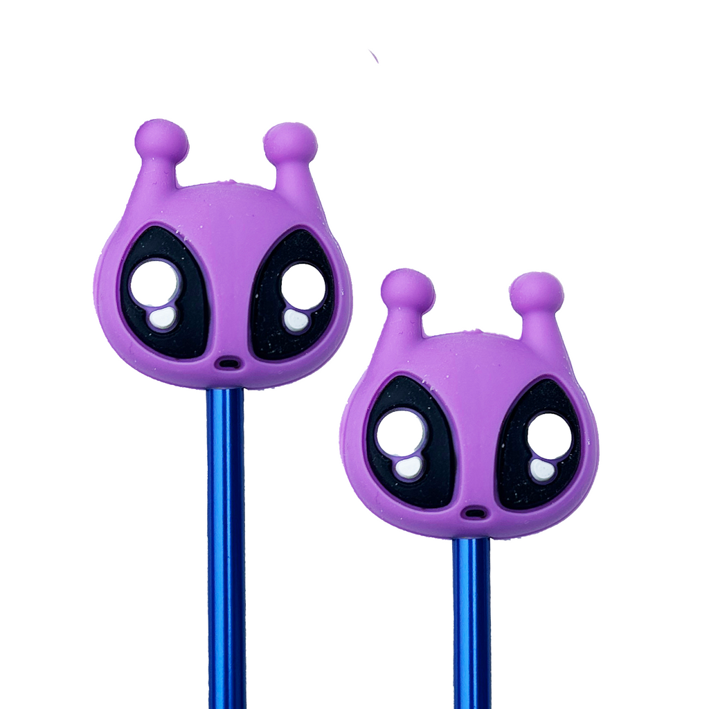 Two purple alien needle point protectors on the end of blue knitting needles on a white background