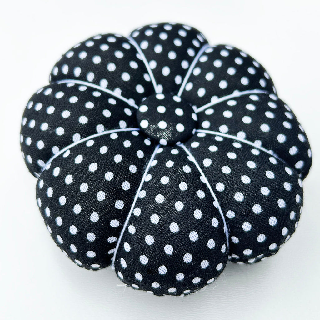 Black polka dot pumpkin-shaped pin cushion on a white surface