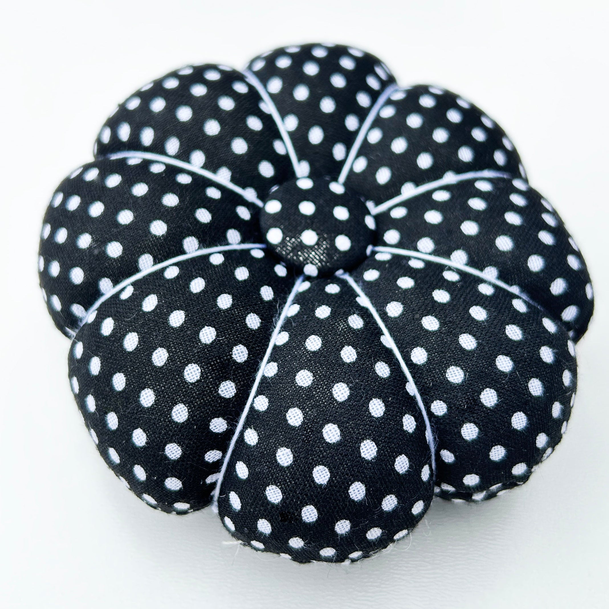 Black polka dot pumpkin-shaped pin cushion on a white surface