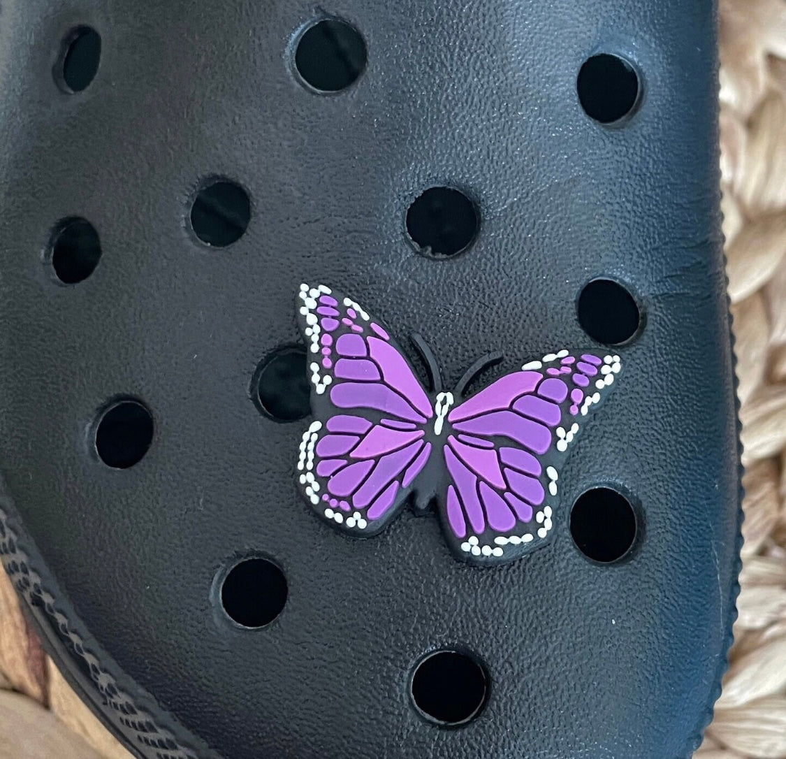 Purple butterfly shoe charm inserted into a hole in a black croc shoe.