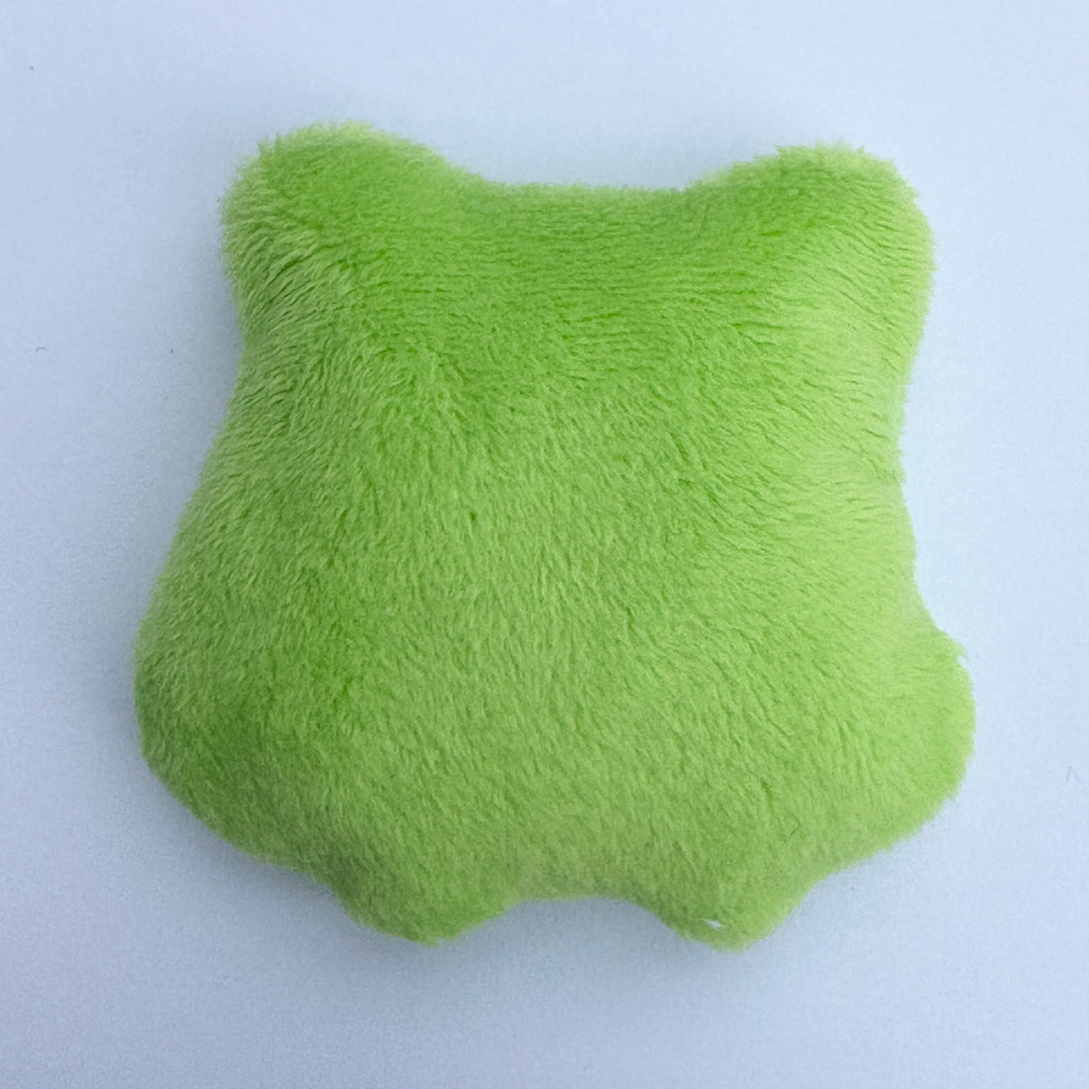 A bright green plush star-shaped pillow shown against a light gray background, with a second cropped green plush toy visible in the bottom right corner.