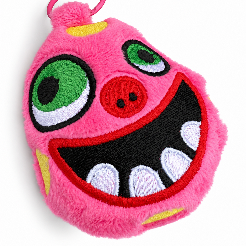 A pink fuzzy monster plush keychain or bag charm with embroidered green eyes, a red mouth with white teeth, and a pink key ring, shown on a white background. Resembles Mr Blobby.