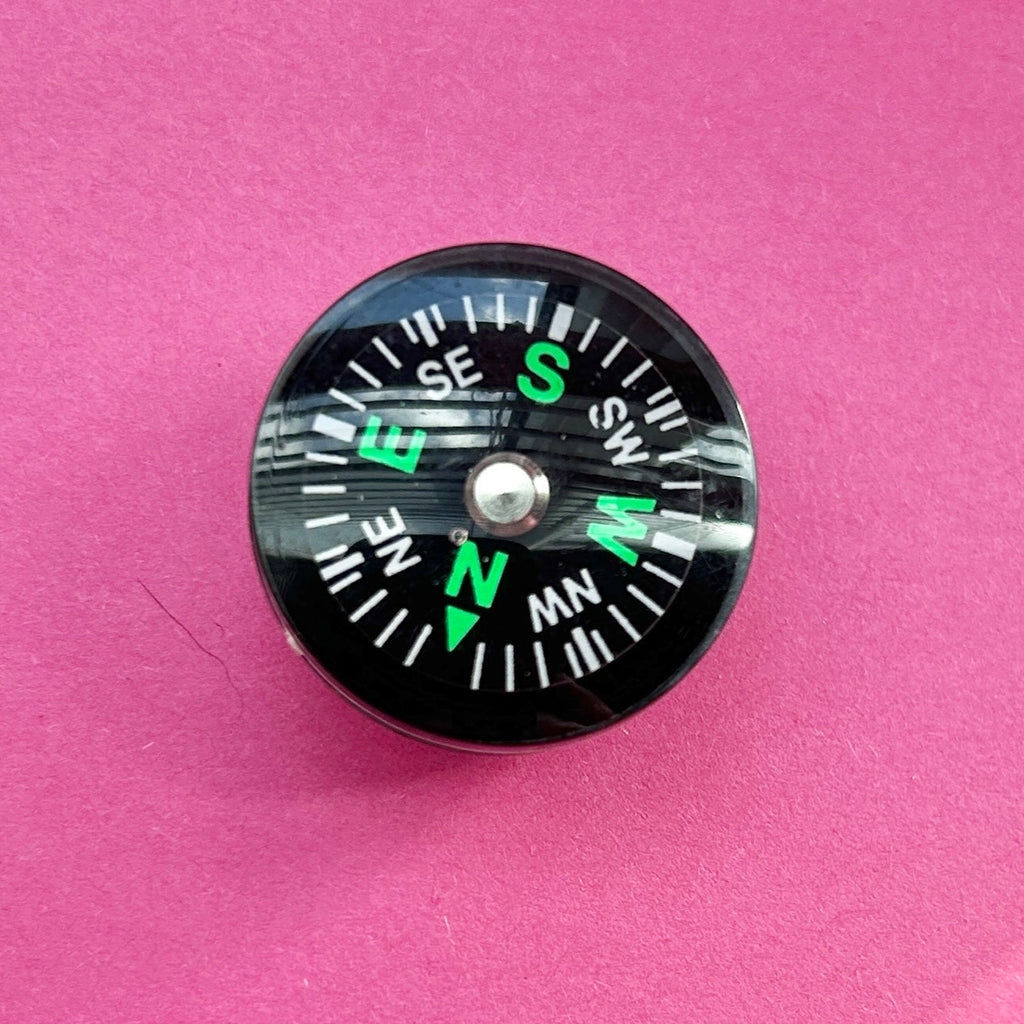 3D working compass croc shoe charm. Shown top down on a pink background.