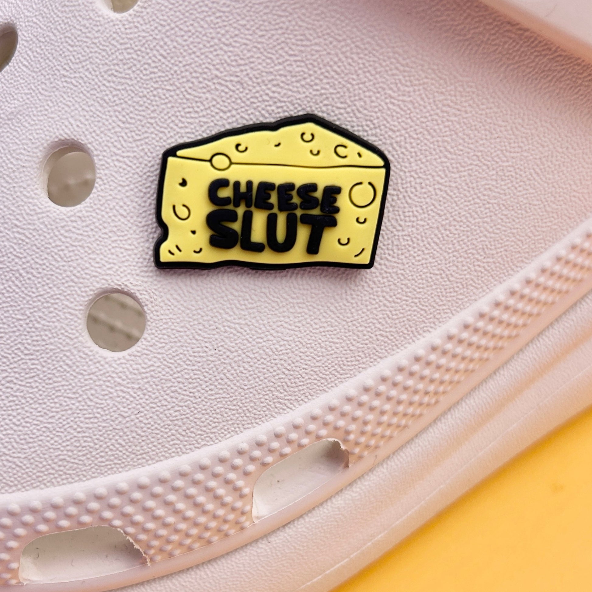 Cheese Slut croc like shoe charm. Yellow and Black. Shown on a cream croc shoe.