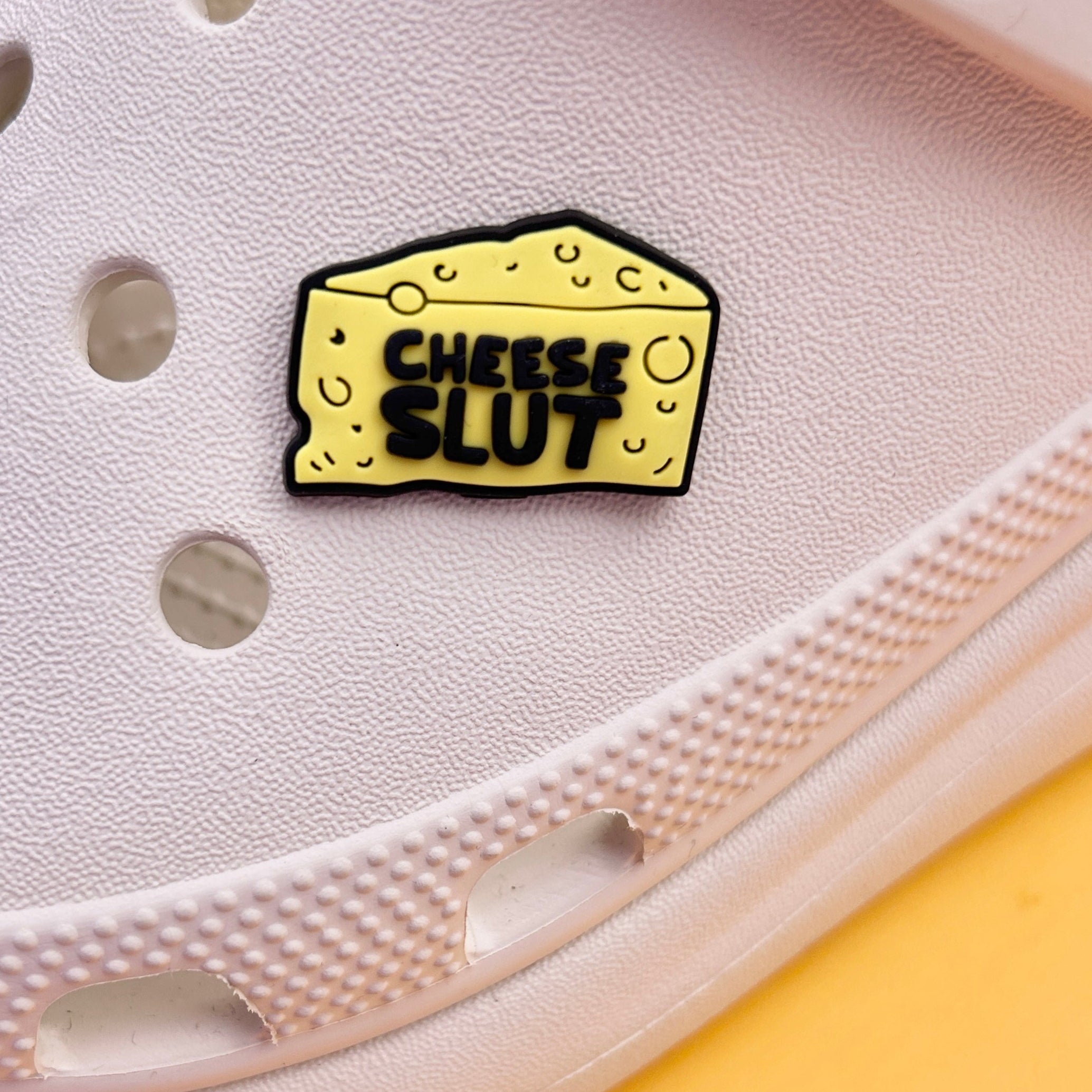 Cheese Slut croc like shoe charm. Yellow and Black. Shown on a cream croc shoe.