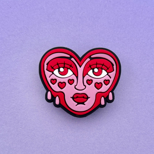 Pink and Red crying face heart croc shoe charm accessory. Photographed on a lilac background. 