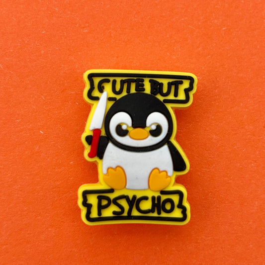 White and Black penguin with the word in black, cute but psycho, holding a knife with a red handle. Yellow background on croc charm. Photographed on an orange background for contrast. 