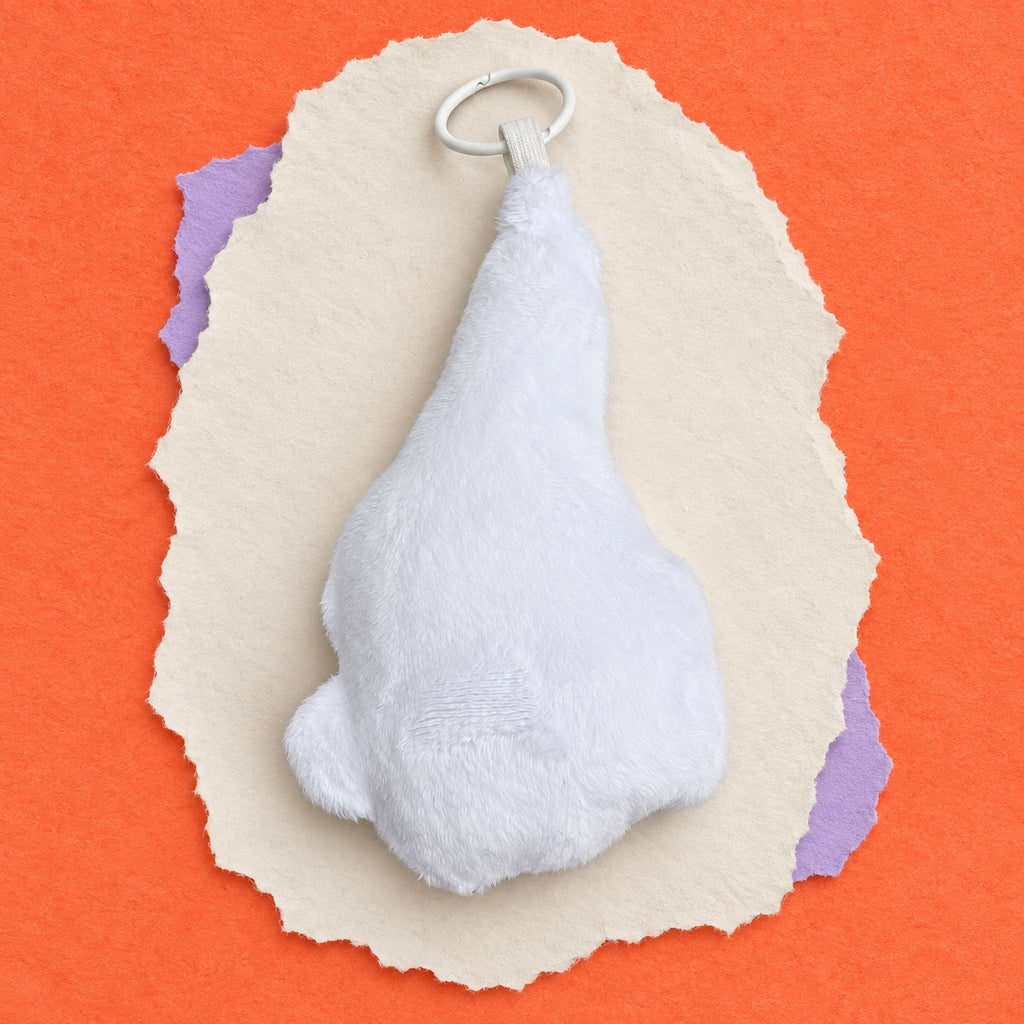 Back view of cockatoo keychain with a silver metal key ring, presented on a styled background of torn beige paper and purple paper over a bright orange surface.