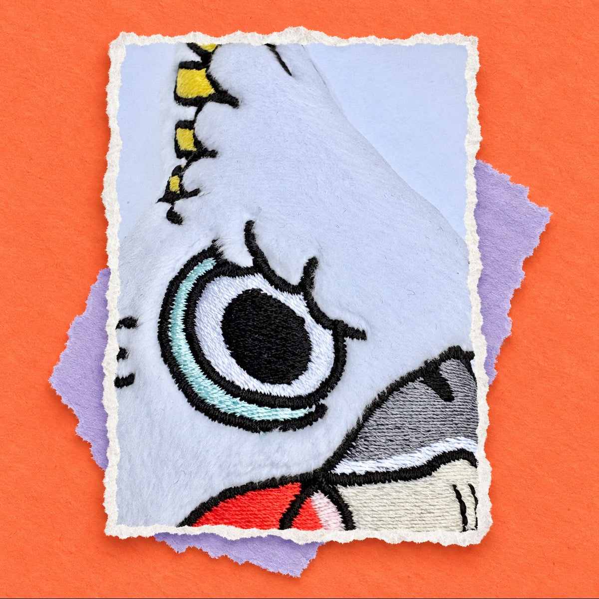 A close-up of a plush Cockatoo with a stylized embroidered eye and stitched details, layered over purple and white fabric pieces on a bright orange background.