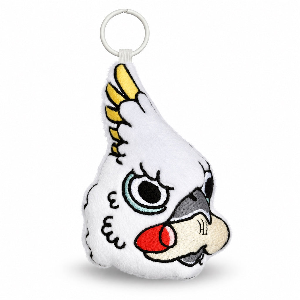 A white plush cockatoo keychain with embroidered details, featuring a white plastic key ring at the top. The cockatoo has yellow feathers on its crest, a red beak, and a gray beak underside, set against a plain white background.