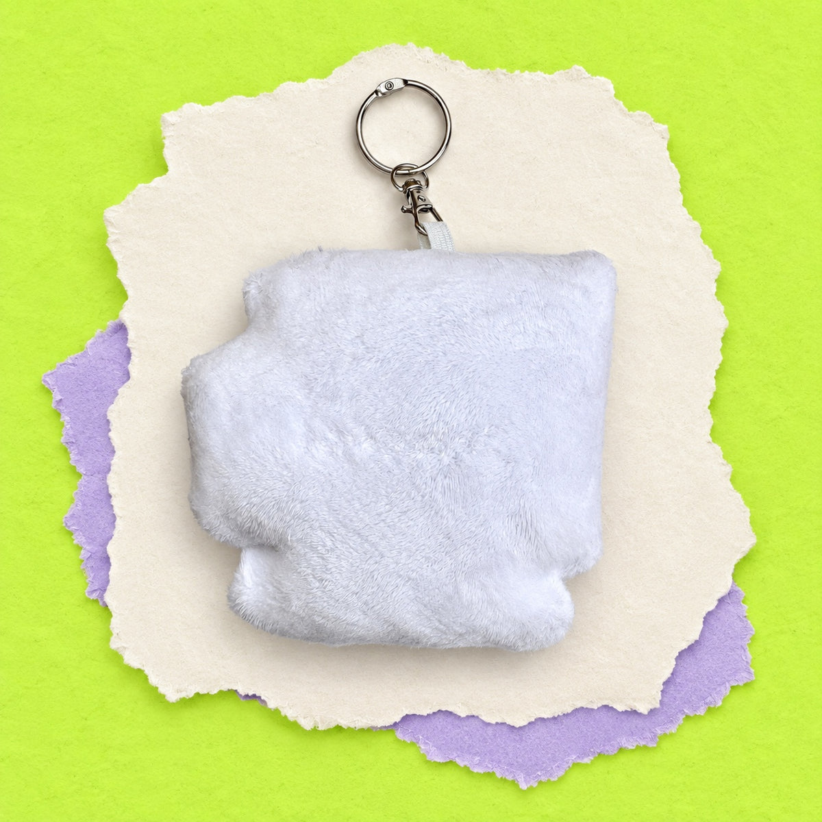 The back of computer pigeon bag charm silver metal split ring, displayed on a stack of torn paper sheets over a bright lime green background.
