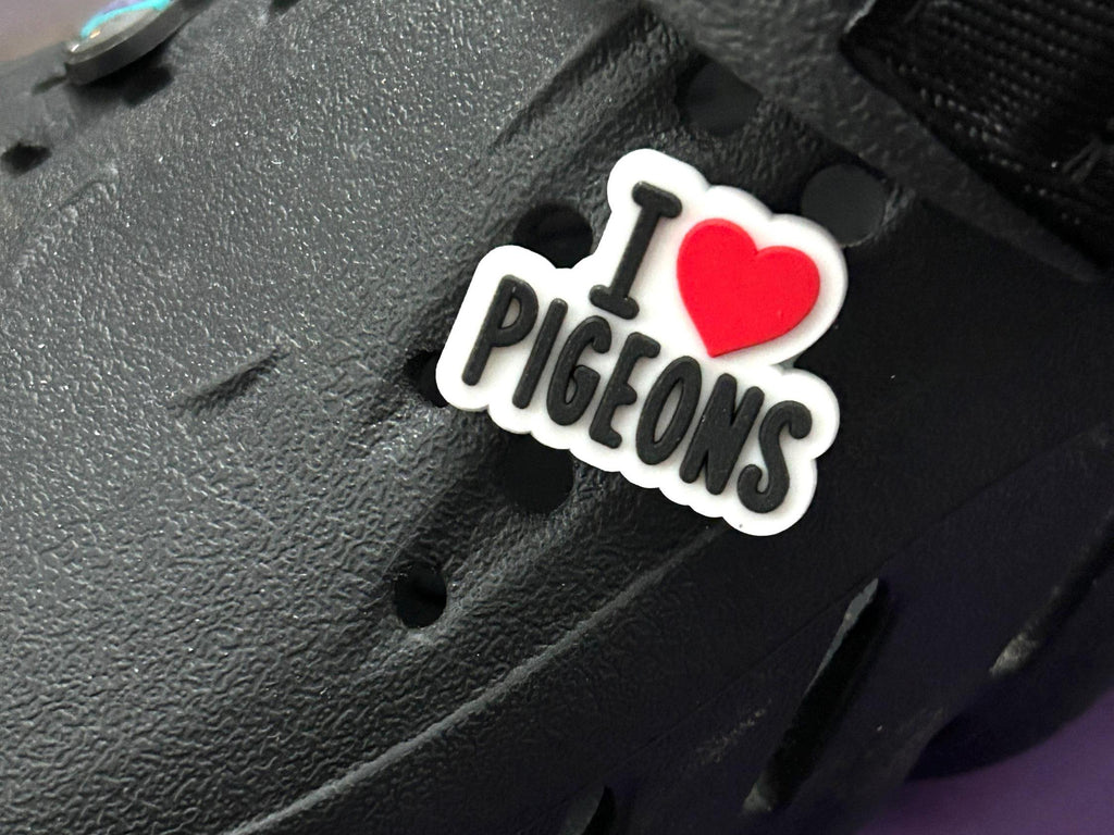 A close-up of a black textured shoe or boot with a white and red sticker that reads 'I [heart] PIGEONS' attached near the center.